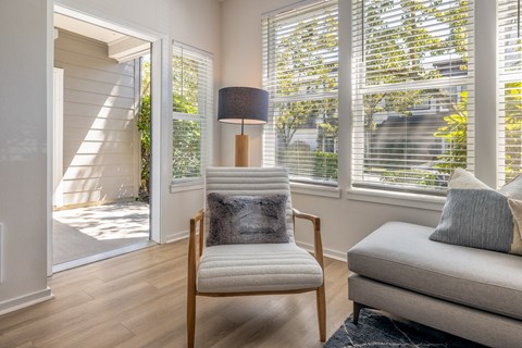 a living room with a chair and a lamp and windows